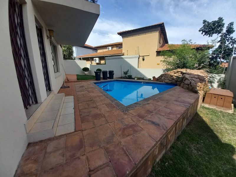 Outdoor pool area featuring a swimming pool with a stone rock feature and tiled surround, adjacent to the main house structure.