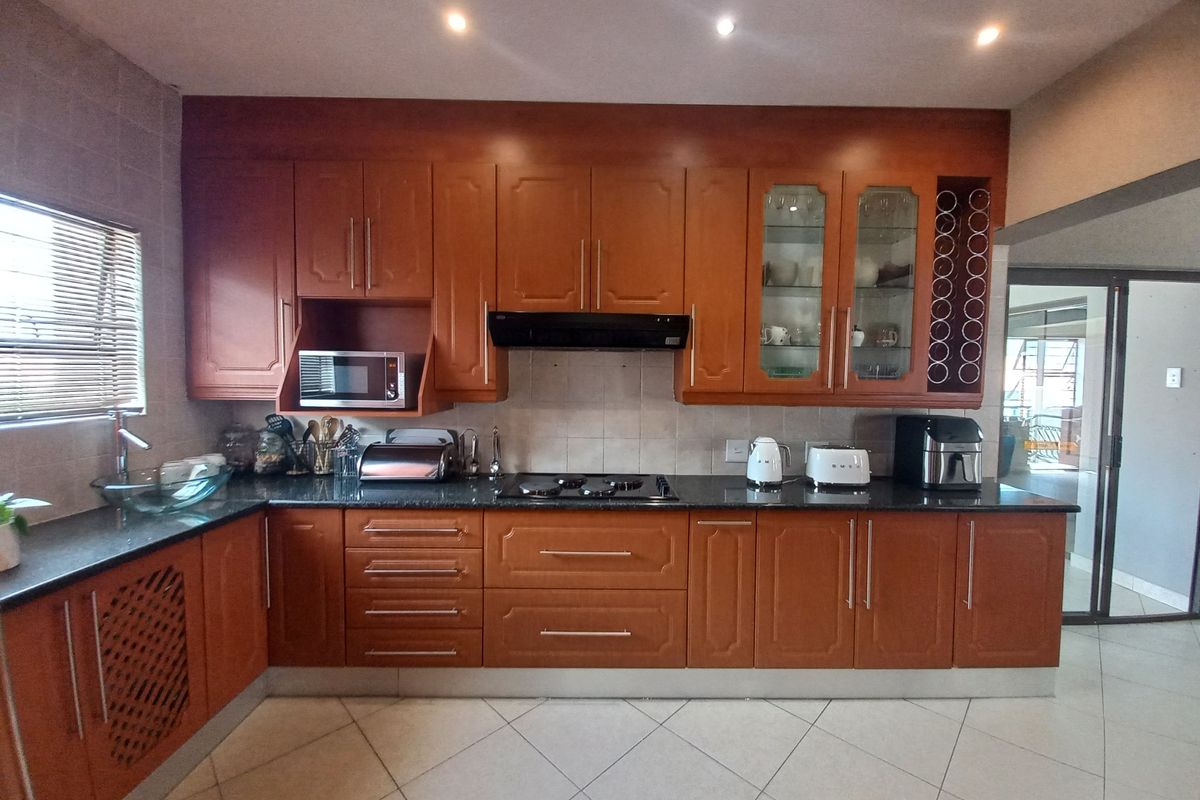 A well-maintained kitchen featuring warm-toned wooden cabinetry, granite countertops, a gas hob, and integrated appliances, offering a functional and classic cooking space.