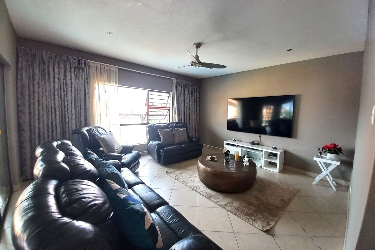 A spacious living room featuring tiled flooring, recessed lighting, a ceiling fan, and large windows allowing for natural light.