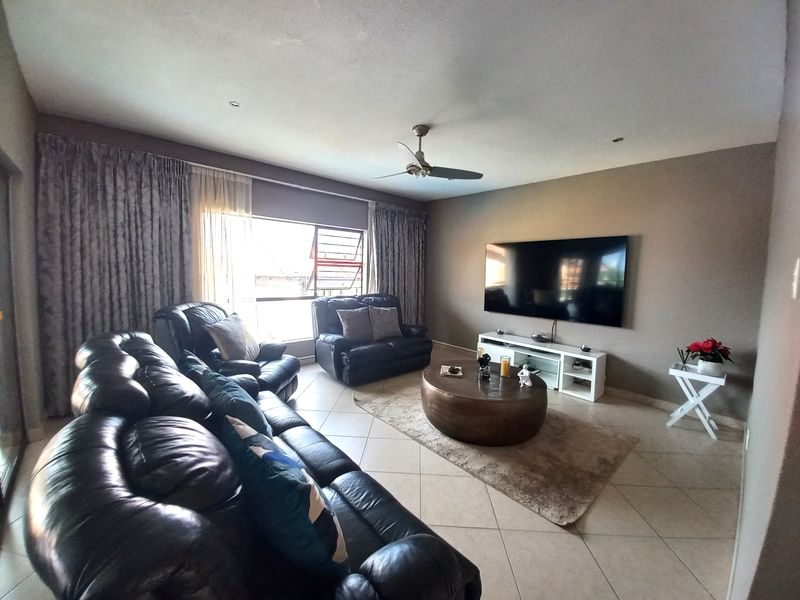 A spacious living room featuring tiled flooring, recessed lighting, a ceiling fan, and large windows allowing for natural light.
