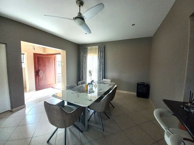 A well-lit dining room featuring tiled flooring, a ceiling fan, and direct access to the entryway.