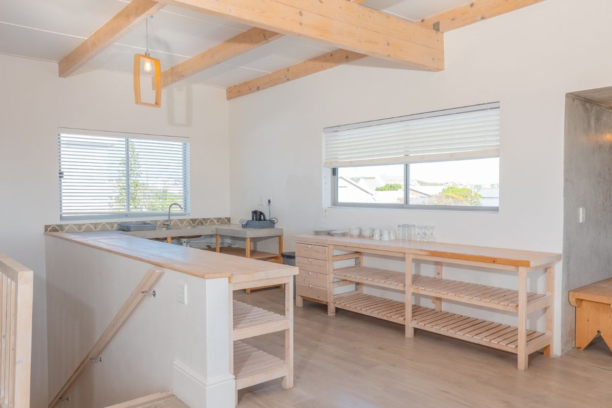 A bright kitchen area featuring exposed timber ceiling beams, custom timber cabinetry, open shelving, and a functional timber countertop workspace.