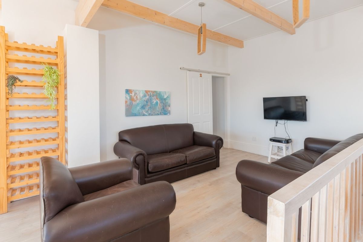A bright living room featuring exposed timber ceiling beams, light laminate flooring, and a timber balustrade overlooking the lower level.