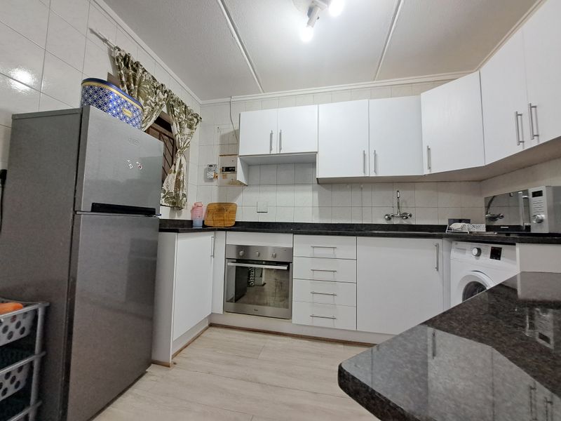 A functional kitchen featuring white cabinetry, dark laminate countertops, tiled backsplash, and built-in oven, providing a practical workspace for daily cooking.