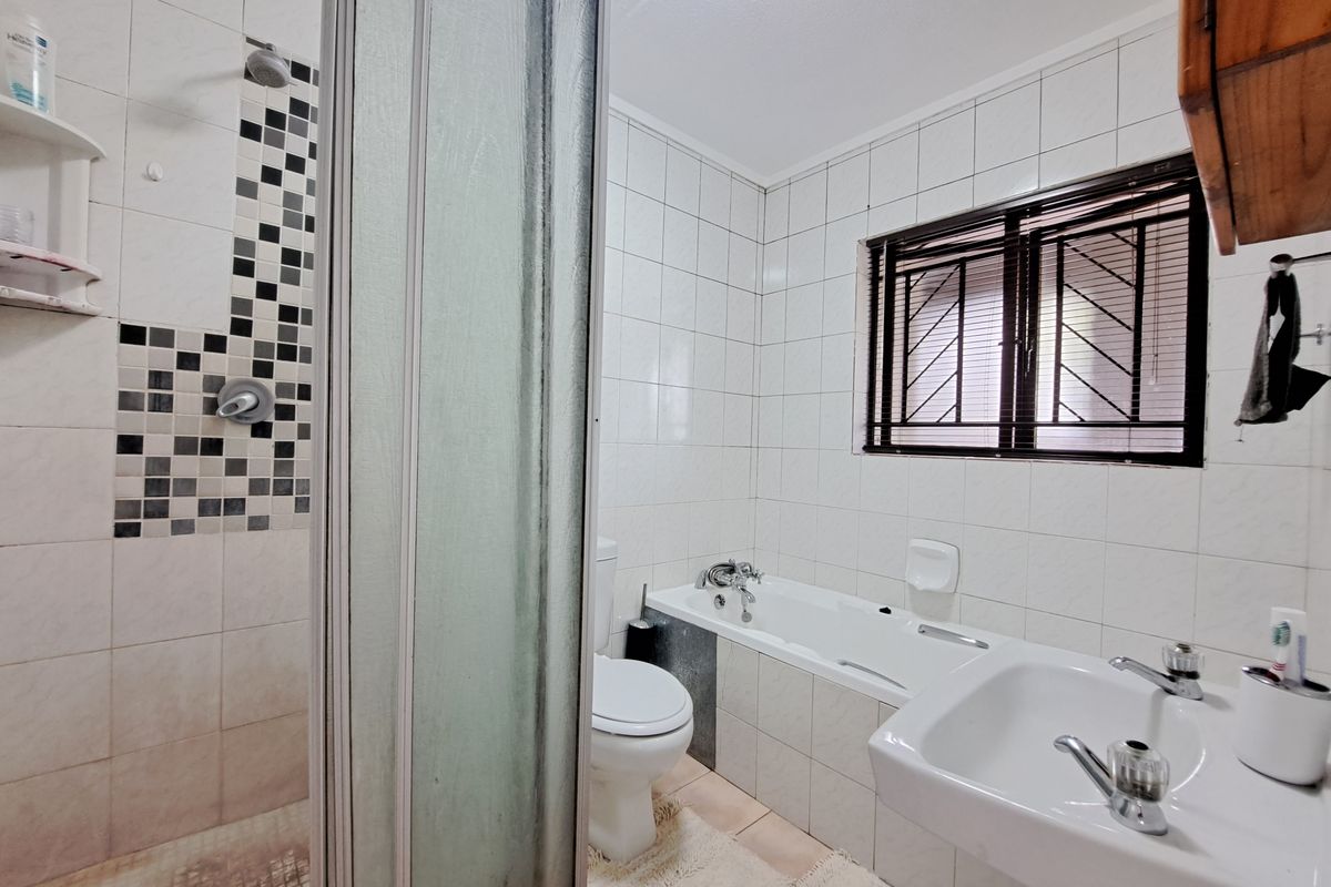 A functional bathroom featuring a shower enclosure, bathtub, pedestal basin, and toilet, finished with white wall tiles and a decorative mosaic accent.