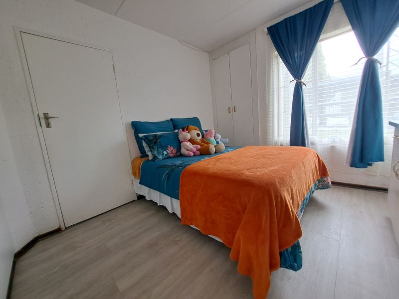 A functional bedroom featuring light-toned laminate flooring and built-in storage cupboards, providing a clean and practical living space.