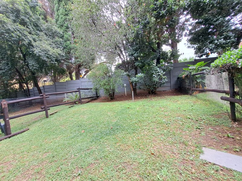A private garden area featuring a lawn, established trees, and secure boundary fencing.