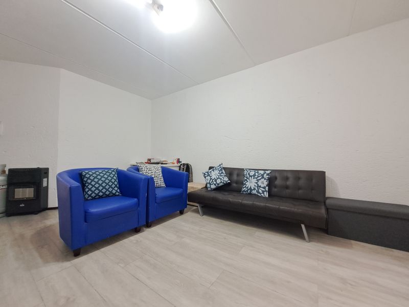 A simple living room area featuring light-toned laminate flooring and textured white walls.
