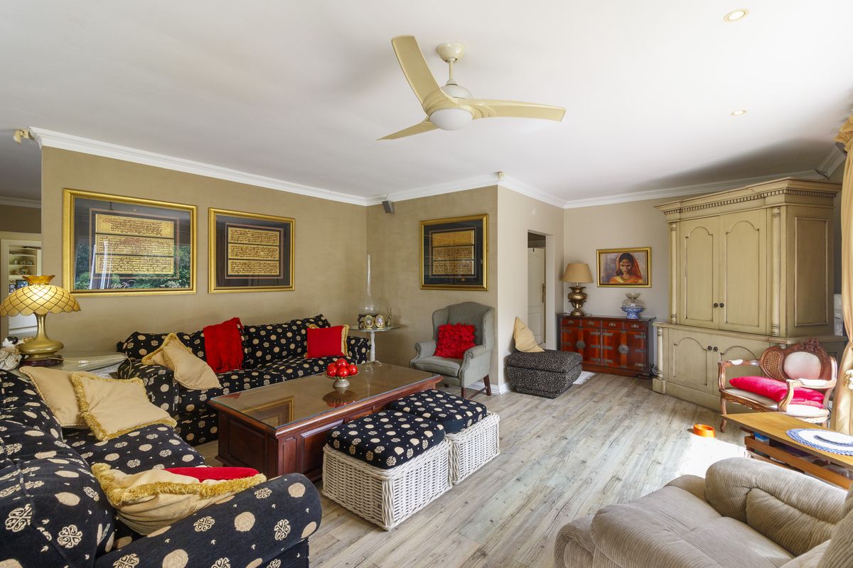 A spacious living room featuring light-toned laminate flooring, crown molding, and a ceiling fan, offering a comfortable and well-maintained living space.