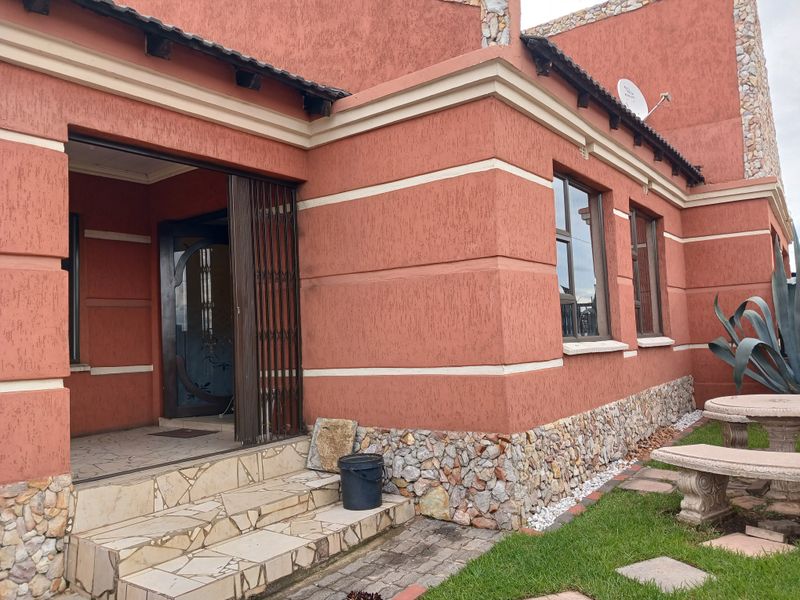 Front entrance view of a house featuring textured plaster walls, stone cladding accents, tiled steps, and a security gate.