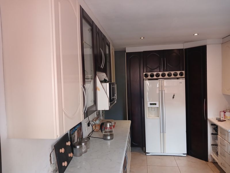 A kitchen featuring two-tone cabinetry, laminate countertops, tiled flooring, and integrated wine storage, showing some signs of wear and unfinished wall detailing.