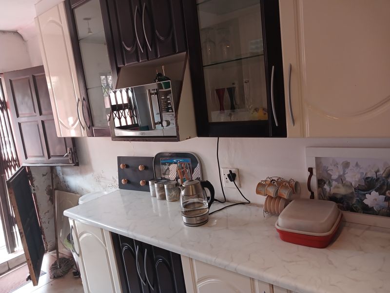 A kitchen area featuring two-tone cabinetry, a laminate countertop, and a built-in microwave, showing signs of wear on the surrounding wall surfaces.