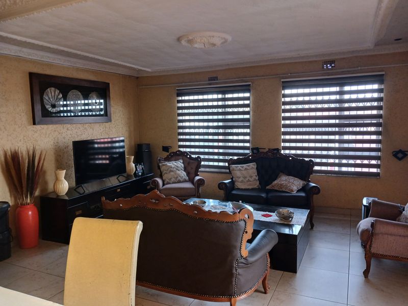 A living room featuring tiled flooring, decorative ceiling rose, detailed cornicing, and modern roller blinds on the windows.