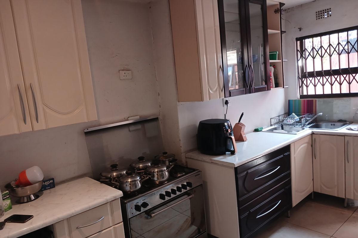 A functional kitchen featuring built-in cabinetry, a freestanding stove, and a stainless steel sink, with visible wear on wall finishes and cabinetry.