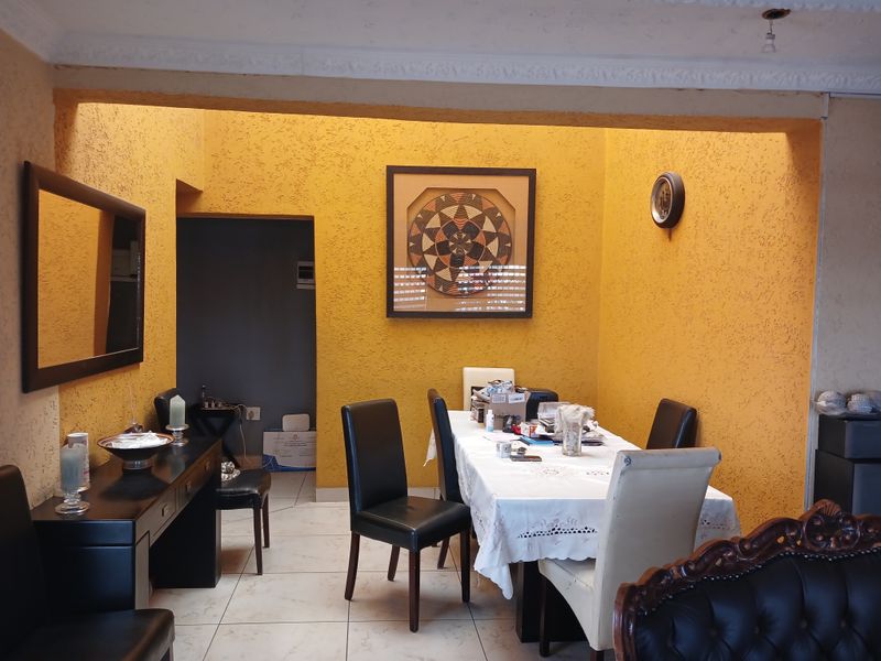 A dining area featuring tiled flooring, textured yellow walls, and decorative ceiling cornicing, providing a functional space for family meals.