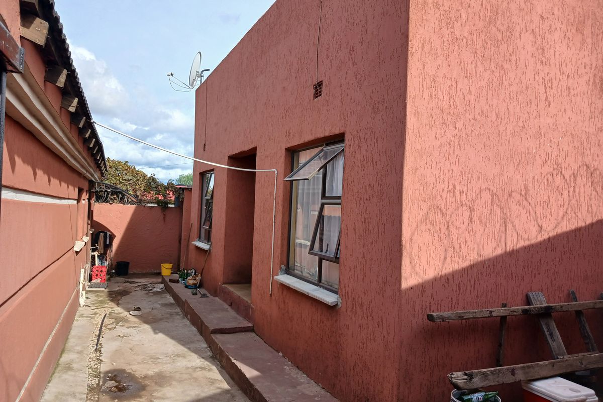 Rear exterior view of the property featuring textured stucco walls, aluminium window frames, and a concrete pathway along the side of the building.