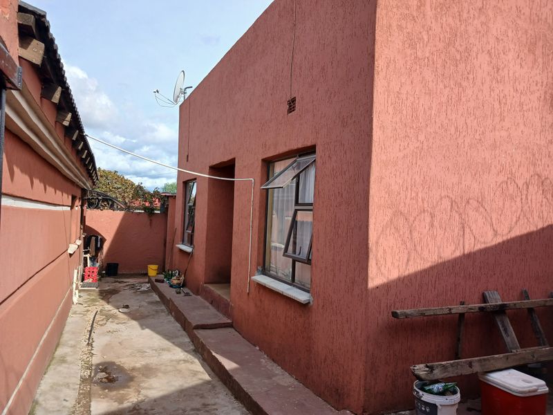 Rear exterior view of the property featuring textured stucco walls, aluminium window frames, and a concrete pathway along the side of the building.