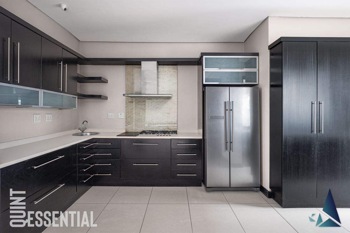 Modern kitchen featuring dark wood cabinetry, stone countertops, stainless steel appliances, and a tiled backsplash in a clean, contemporary layout.