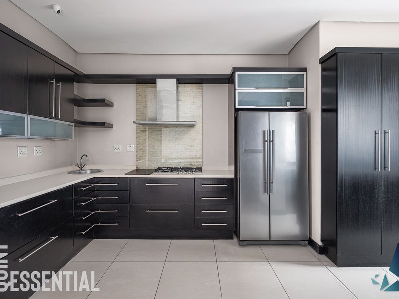 Modern kitchen featuring dark wood cabinetry, stone countertops, stainless steel appliances, and a tiled backsplash in a clean, contemporary layout.