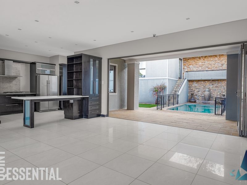 Spacious open-plan kitchen and living area featuring modern cabinetry, tiled floors, and seamless indoor-outdoor flow to a private patio and swimming pool.