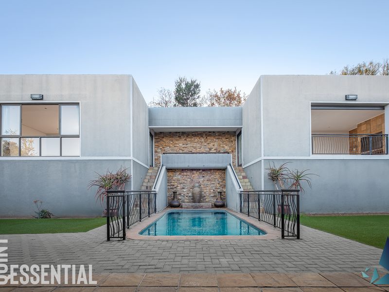 A modern rear exterior featuring a swimming pool, stone feature wall, paved patio area, and manicured artificial lawn.