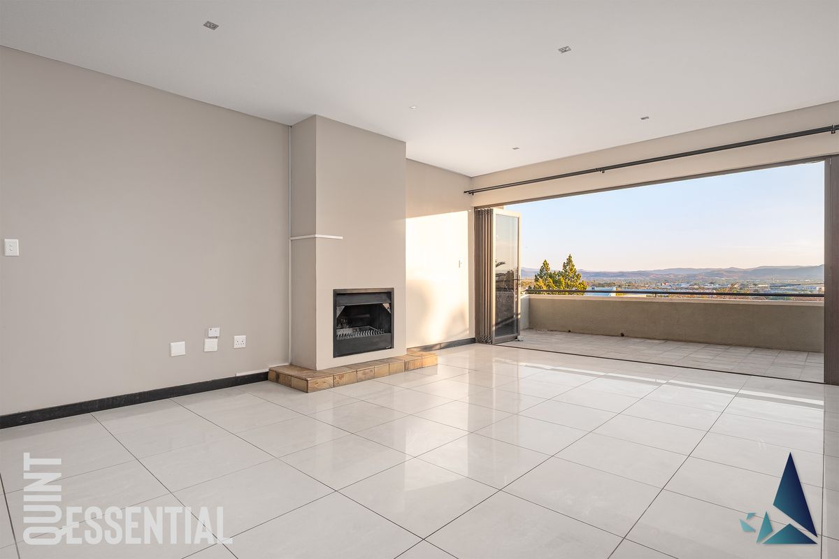 Spacious open-plan living area featuring large format floor tiles, a built-in fireplace, and seamless access to a balcony with expansive views.