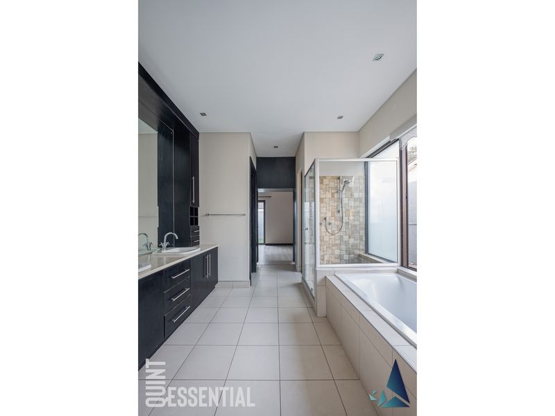 Modern bathroom featuring a double vanity with dark cabinetry, a separate shower enclosure, and a built-in bathtub with neutral floor tiling.