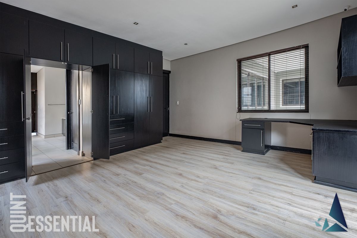 Spacious bedroom featuring modern laminate flooring, extensive built-in dark cabinetry, a built-in desk, and recessed lighting, offering a clean and functional living space.