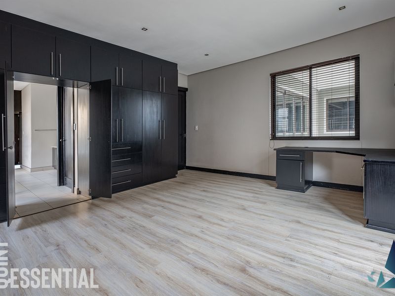 Spacious bedroom featuring modern laminate flooring, extensive built-in dark cabinetry, a built-in desk, and recessed lighting, offering a clean and functional living space.