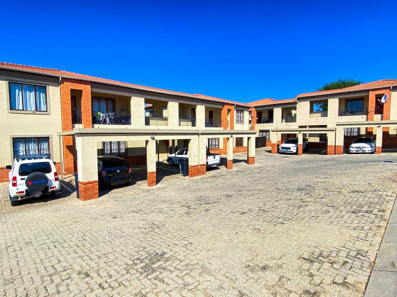 Exterior view of a multi-story apartment complex featuring paved parking areas, covered carports, and brick-accented building facades.