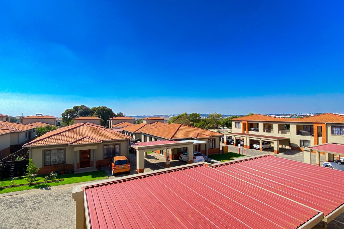 An elevated aerial view of a residential apartment complex featuring tiled roofs, paved driveways, and covered carports within a well-maintained estate.
