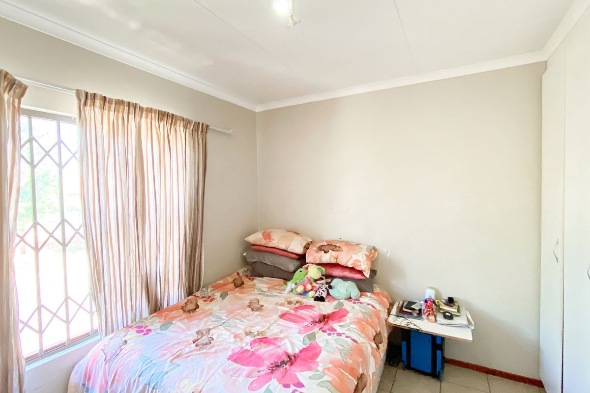 A functional bedroom featuring built-in cupboards, tiled flooring, and a window fitted with a security gate.