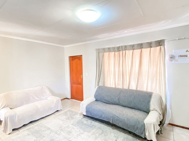 A simple living room featuring tiled flooring, a central ceiling light, and a wall-mounted electrical distribution board.
