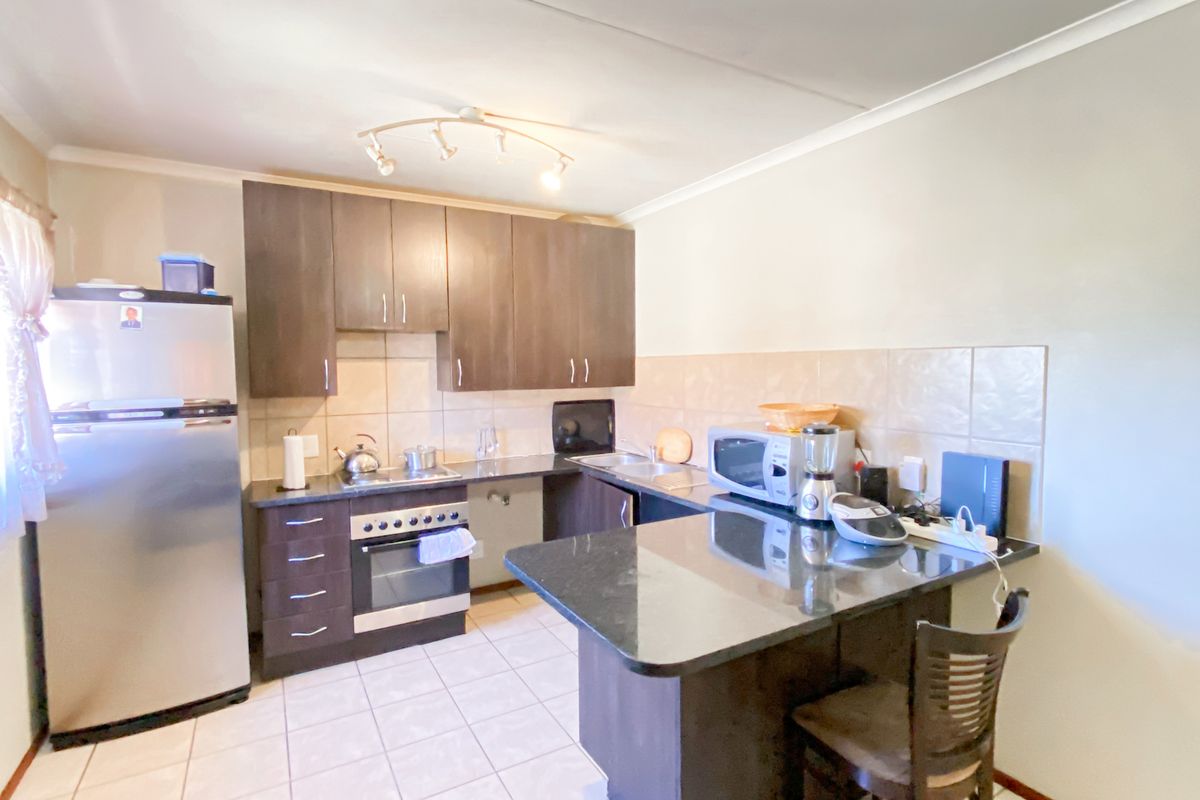 A functional kitchen featuring dark wood cabinetry, granite countertops, a built-in oven, hob, and a convenient breakfast nook with tiled flooring.