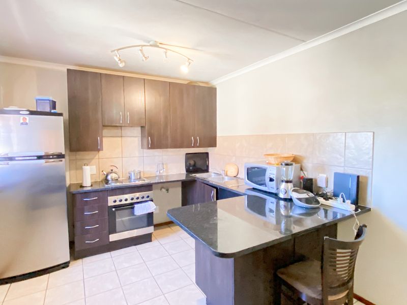 A functional kitchen featuring dark wood cabinetry, granite countertops, a built-in oven, hob, and a convenient breakfast nook with tiled flooring.