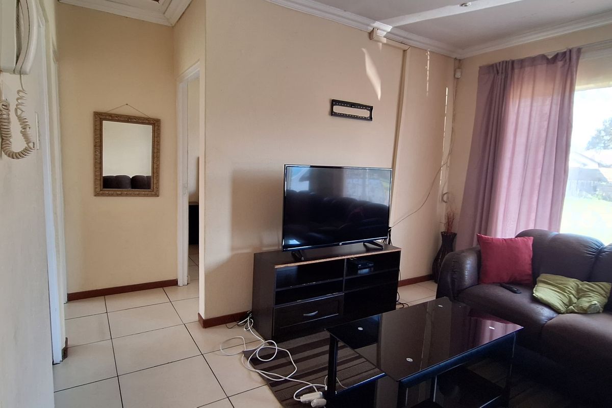 A living room featuring tiled flooring, large windows for natural light, and an intercom system, requiring some cosmetic updates to the walls and electrical finishes.