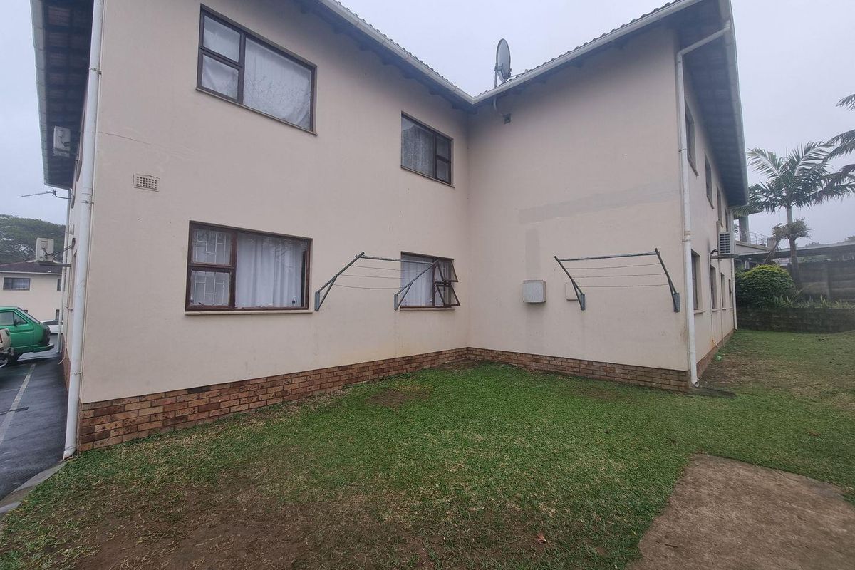 Rear exterior view of the apartment building featuring a small lawn area, wall-mounted drying racks, and standard window placements.