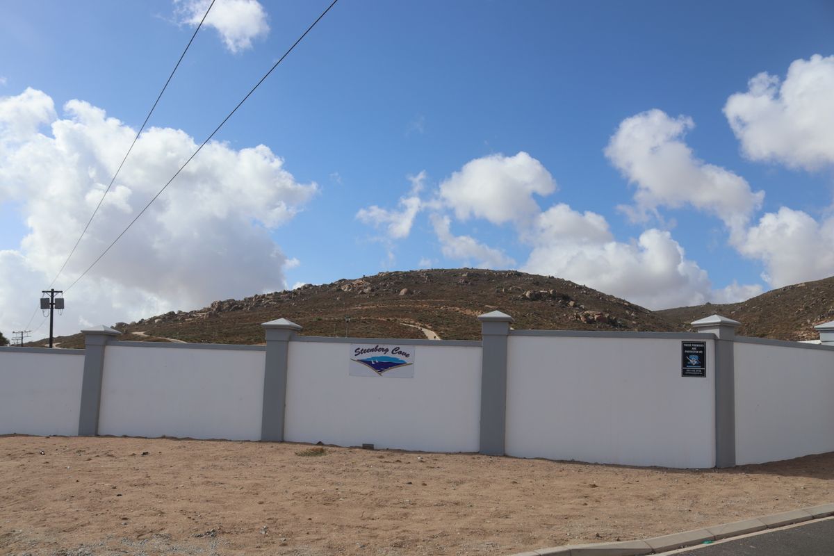 A view of the perimeter wall and entrance signage for the Steenberg Cove residential development, set against a hilly landscape.