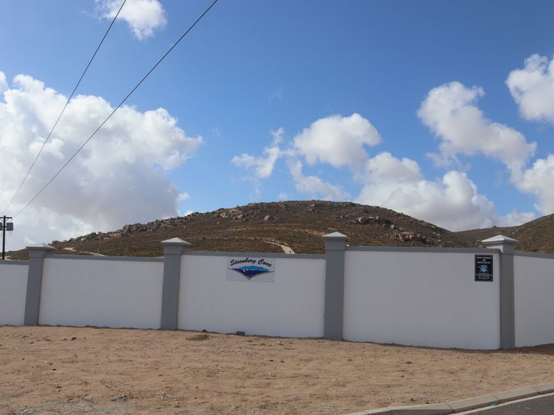 A view of the perimeter wall and entrance signage for the Steenberg Cove residential development, set against a hilly landscape.