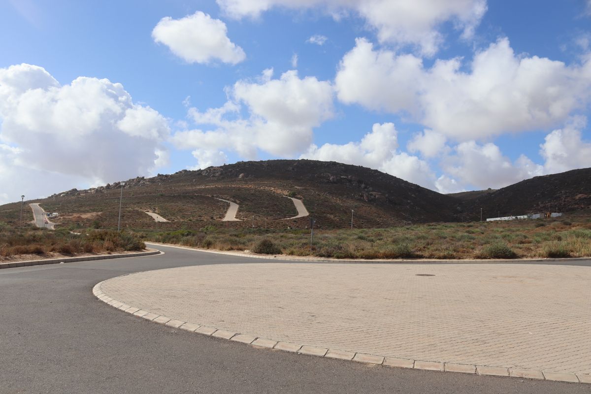 A view of a paved cul-de-sac and road infrastructure within a residential development, featuring surrounding hilly landscape and clear skies.