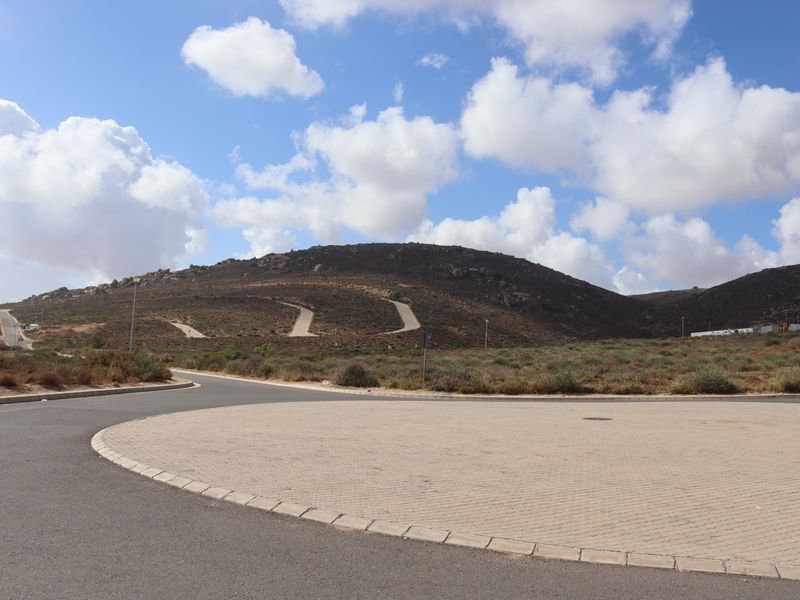 A view of a paved cul-de-sac and road infrastructure within a residential development, featuring surrounding hilly landscape and clear skies.