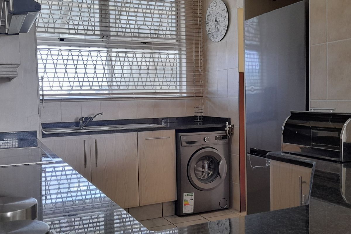 A functional kitchen featuring granite countertops, built-in cabinetry, tiled backsplash, and a window with a security gate.