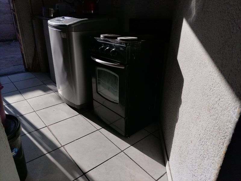 A functional laundry area featuring tiled flooring and a freestanding stove, requiring cosmetic updates to improve the overall aesthetic and brightness.