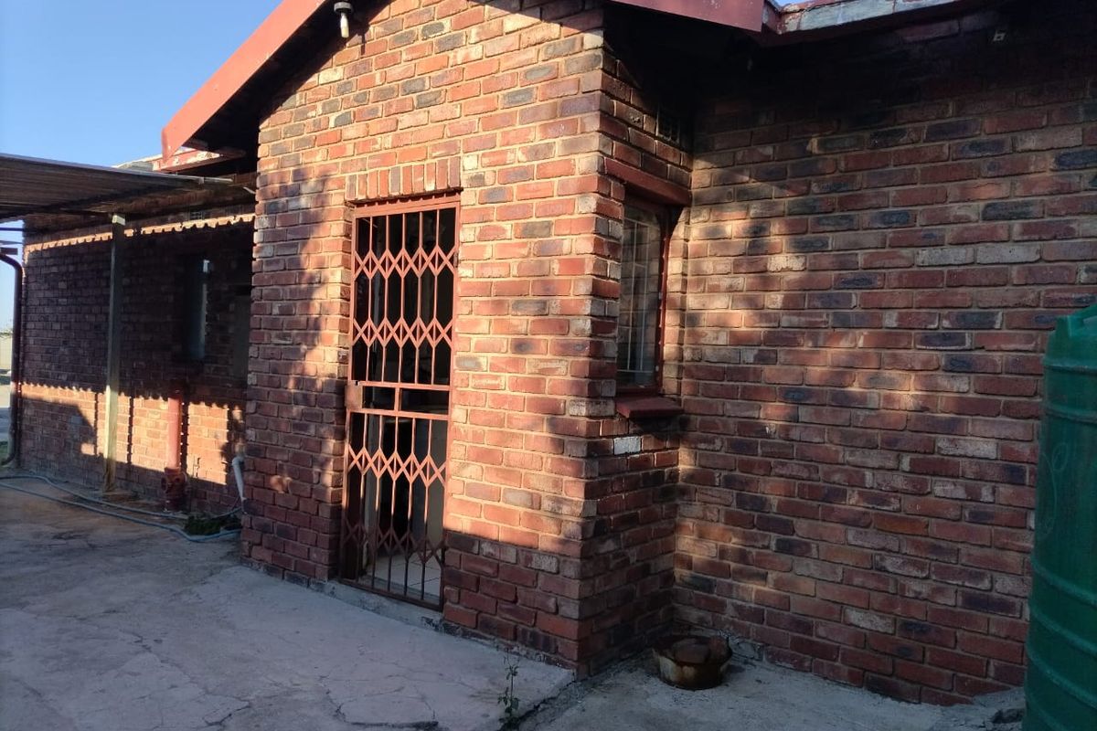 A view of the rear exterior featuring face brick walls, a security gate, and a concrete patio area with an adjacent water tank.