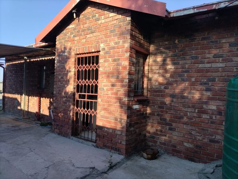 A view of the rear exterior featuring face brick walls, a security gate, and a concrete patio area with an adjacent water tank.