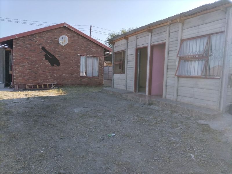 Rear view of the property showing a brick structure and a secondary precast concrete building with security bars on the windows.