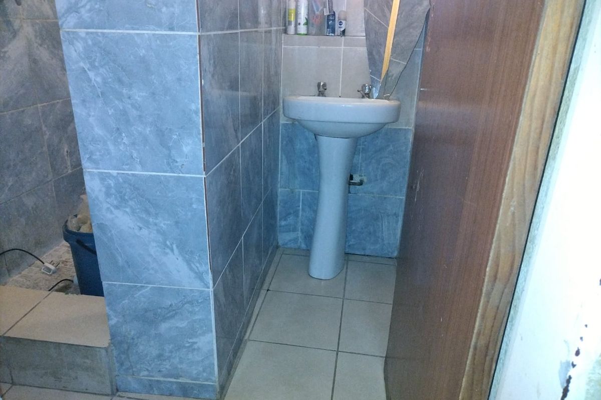 A small bathroom featuring a pedestal basin and tiled finishes, currently showing signs of wear and incomplete wall tiling.