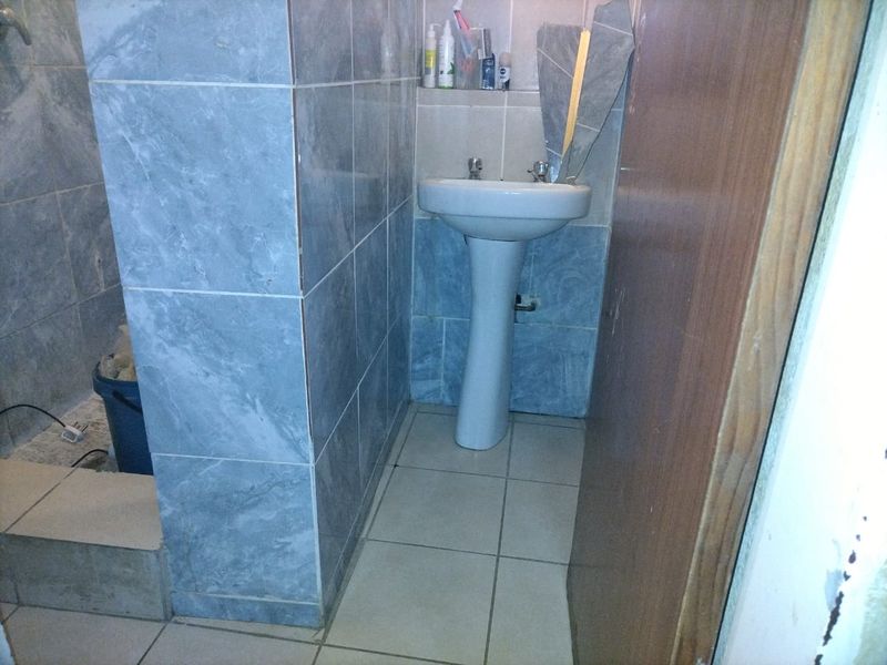 A small bathroom featuring a pedestal basin and tiled finishes, currently showing signs of wear and incomplete wall tiling.