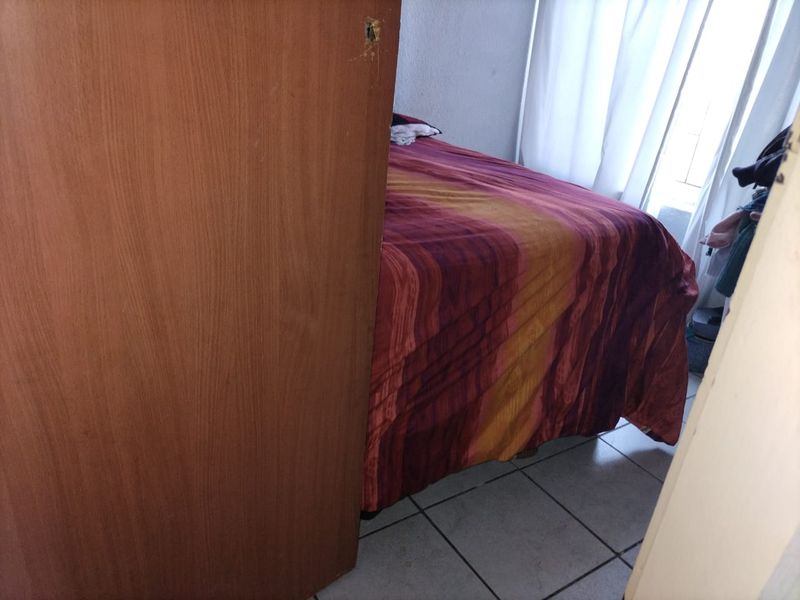 A bedroom featuring tiled flooring, captured from a restricted angle through a doorway with visible damage to the door frame.