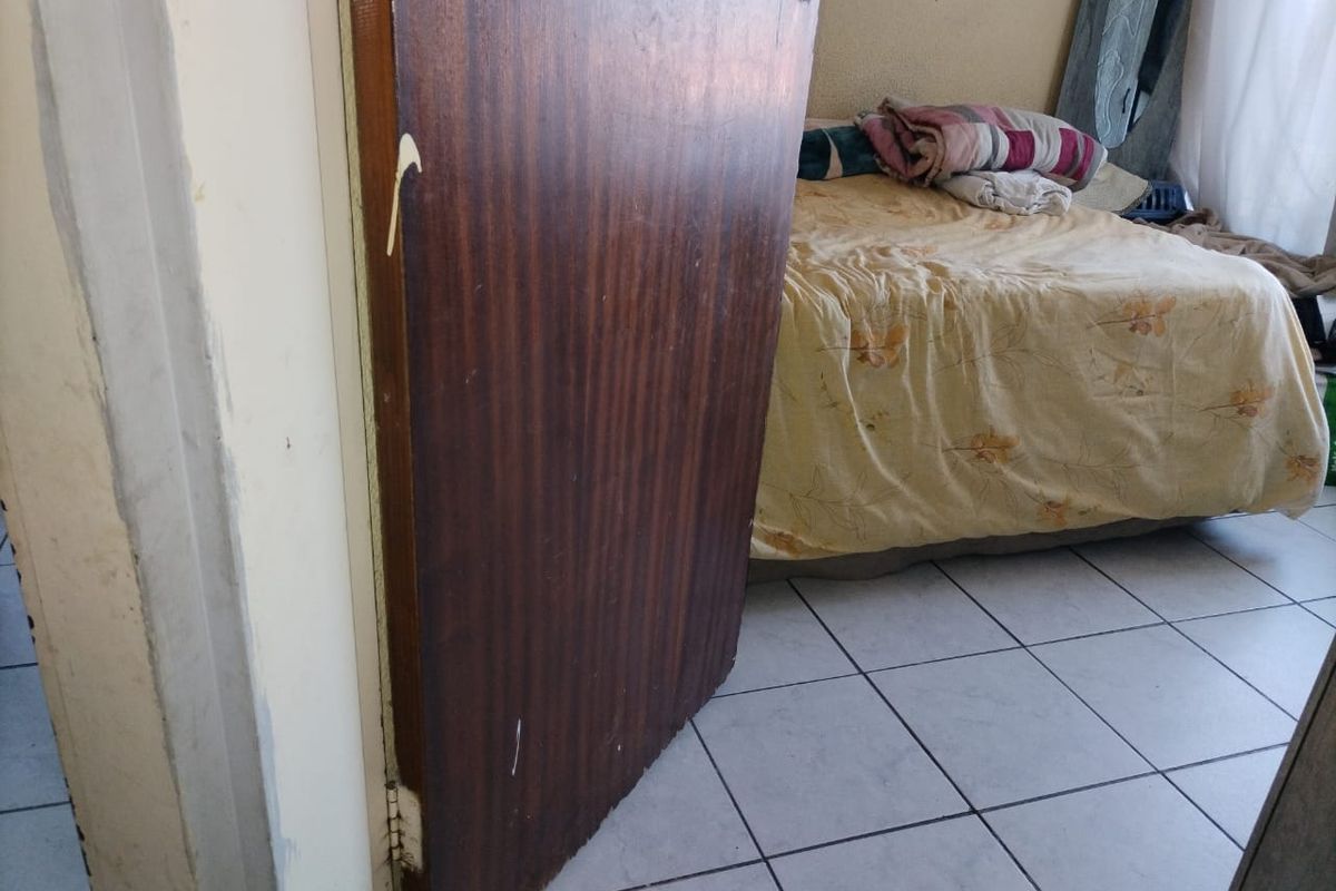 A bedroom featuring tiled flooring and a wooden door, currently showing signs of wear and tear on the door and frame.